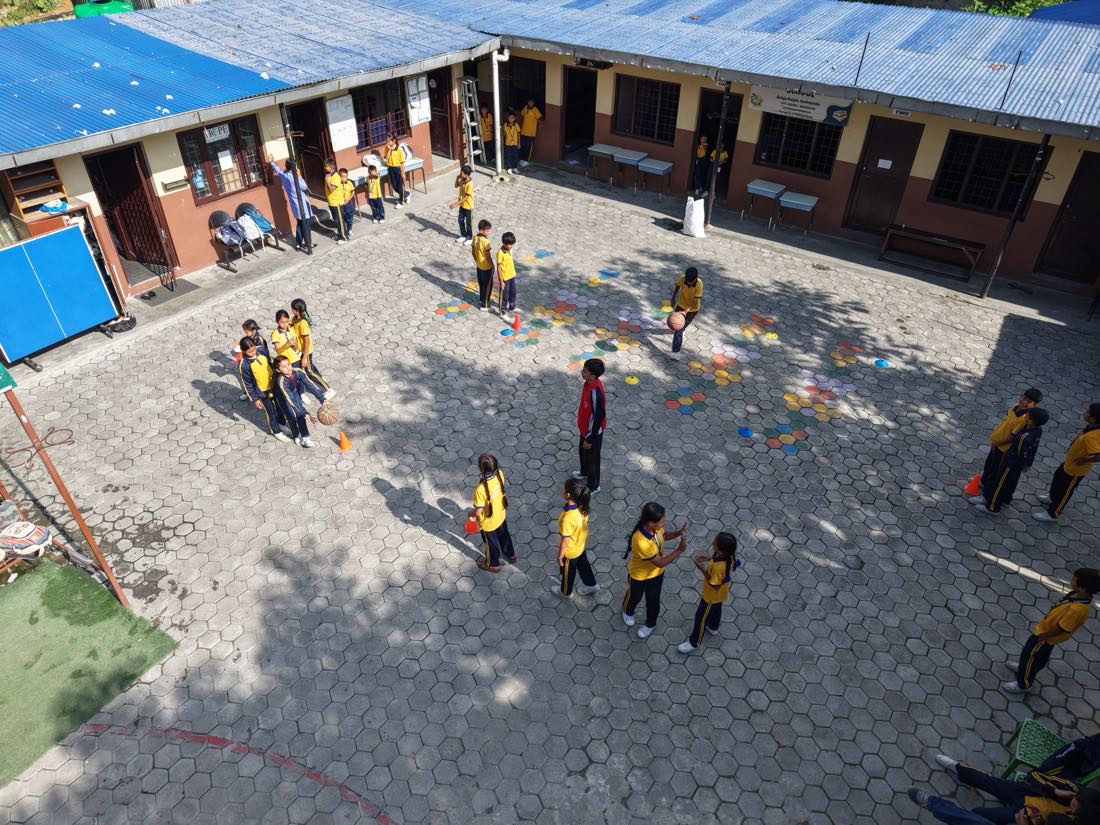 Children in yellow uniforms playing in a paved schoolyard, seen from above