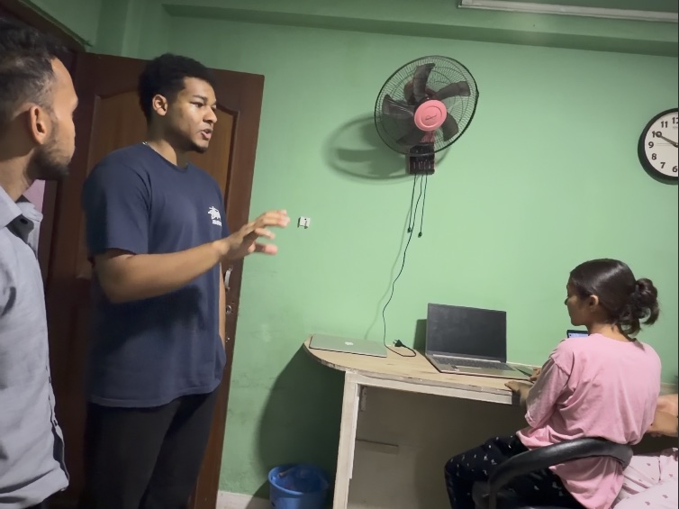 Shawn standing and explaining something to a student working at a laptop in a green-walled classroom